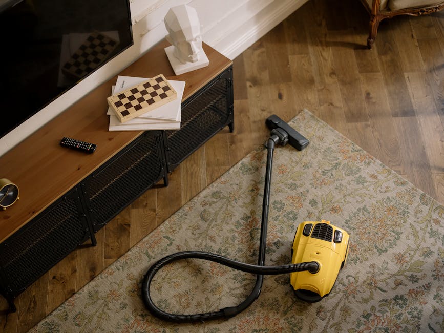 A low-angle view of a hallway with a textured carpeted floor in a residential property, bordered by white wooden wainscoting and wallpaper with vertical black and white stripes. The corridor is illumi